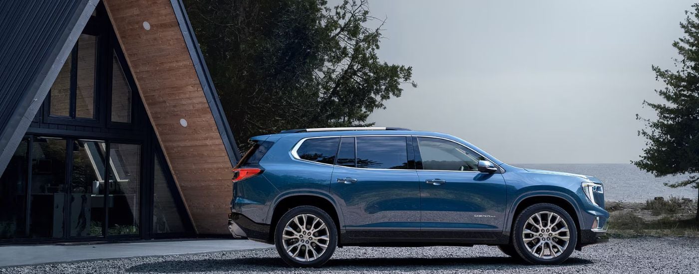 Blue 2026 GMC Acadia Denali parked outside a lakeside cabin.