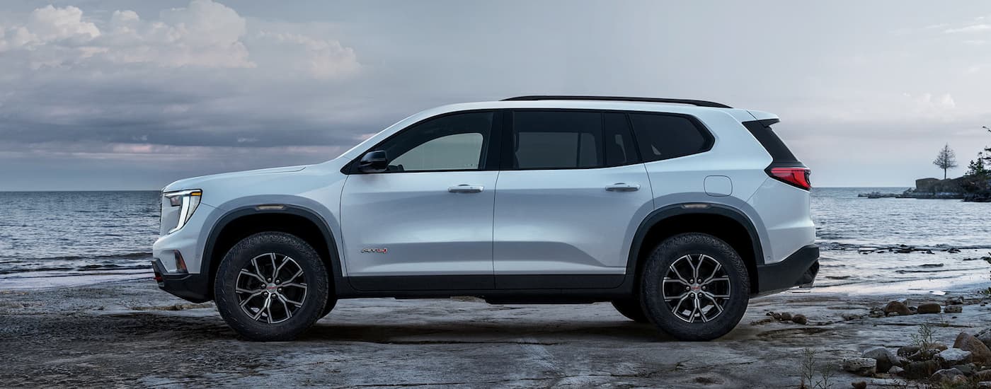 Side of a white 2026 GMC Acadia AT4 parked by a lake.
