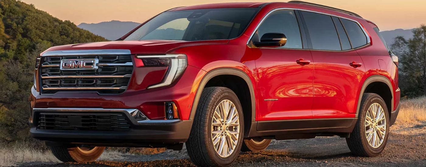Red 2026 GMC Acadia driving on a dirt trail.