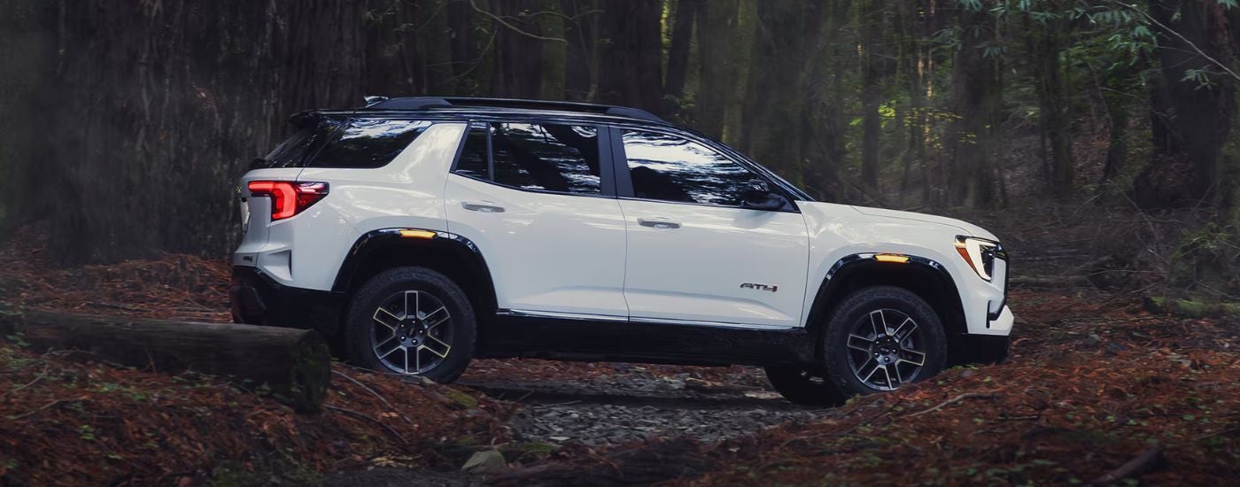 White 2026 GMC Terrain AT4 from the side driving through the forest.